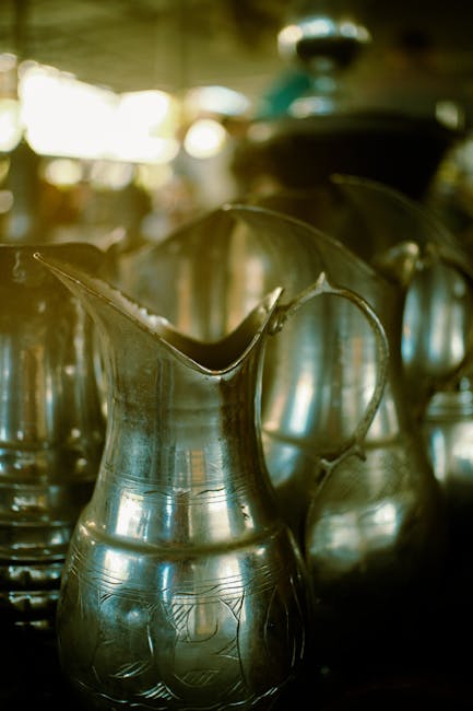 A row of vintage metal pitchers displayed under warm ambient lighting, exuding a classic feel.